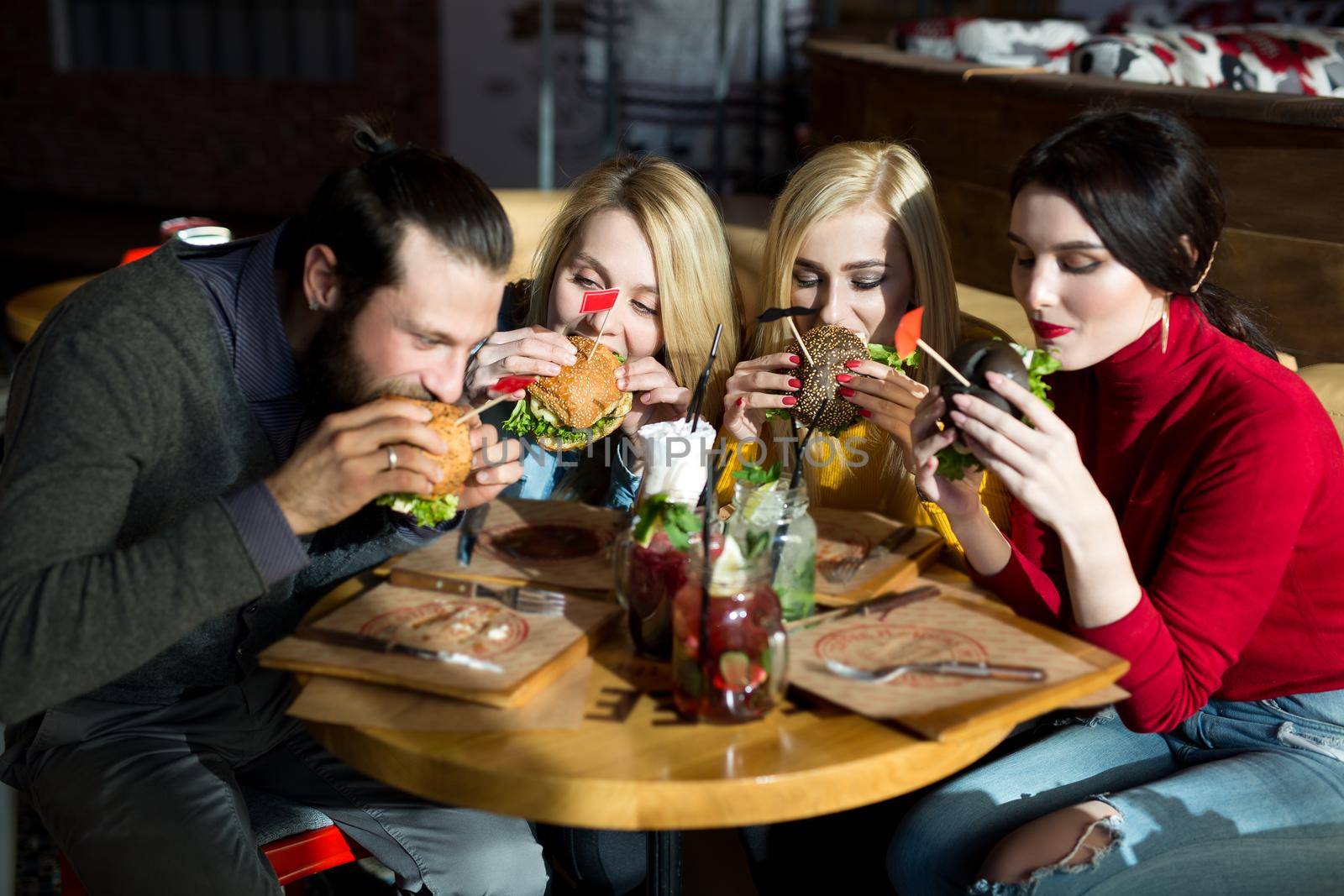 People have dinner together at a table in a cafe. Happy friends eat burgers and have fun by StudioPeace