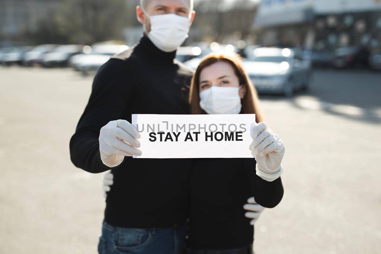 A woman and a man in protective medical masks hold a placard reading stay at home. Message for prevention of bovine coronavirus-19.
