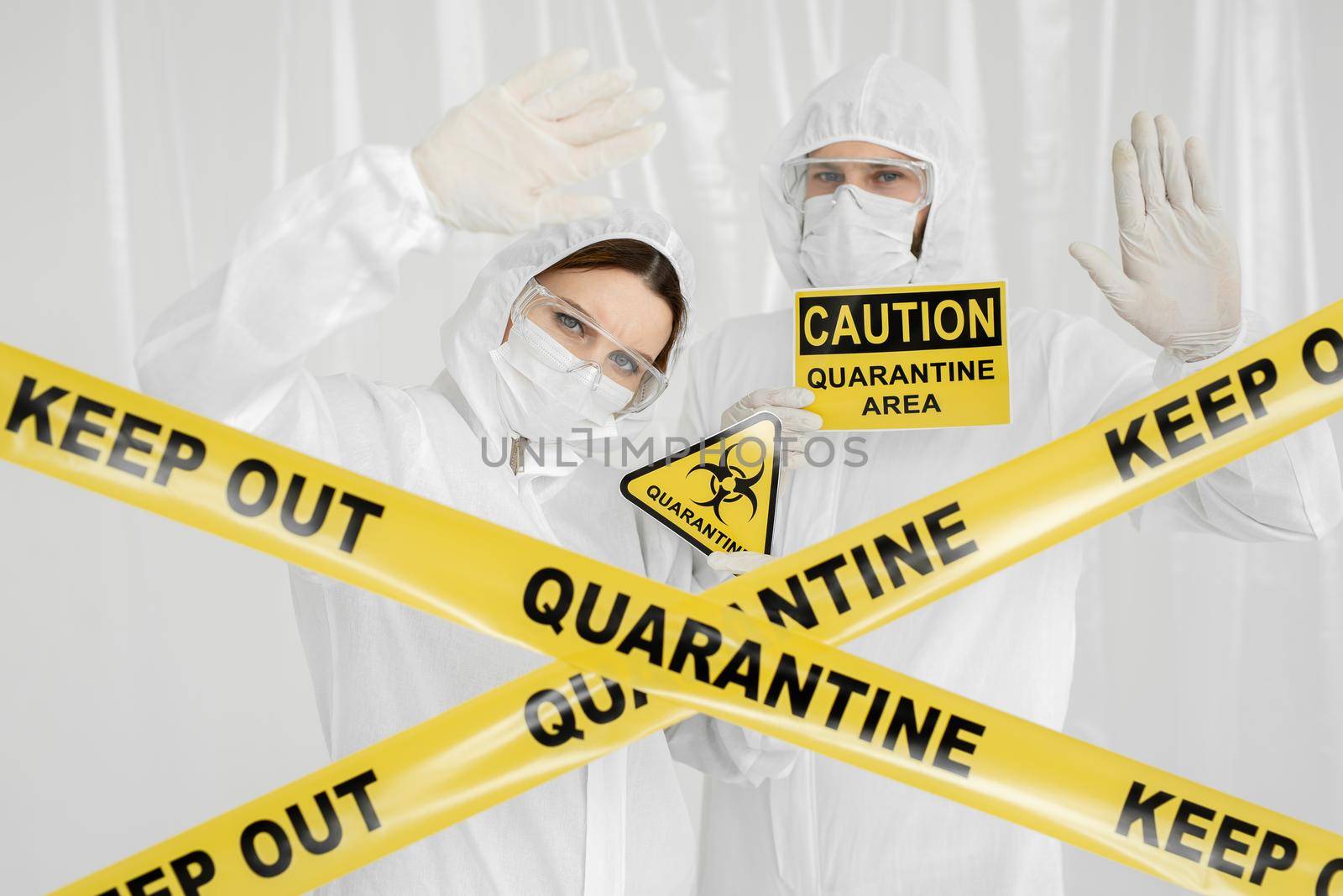 Epidemiologists a man and a woman in protective clothing are in a restricted area with a danger sign. Yellow line Keep Out Quarantine. Quarantine alert sign. Entrance is forbidden in quarantine zone