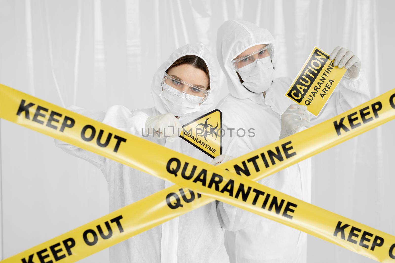 Epidemiologists a man and a woman in protective clothing are in a restricted area with a danger sign. Yellow line Keep Out Quarantine. Quarantine alert sign. Entrance is forbidden in quarantine zone. by StudioPeace