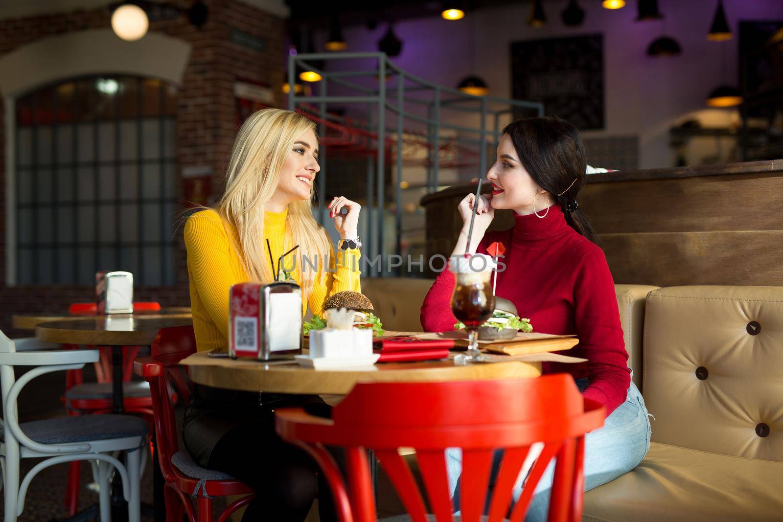 Two young women chatting in a cafe. by StudioPeace