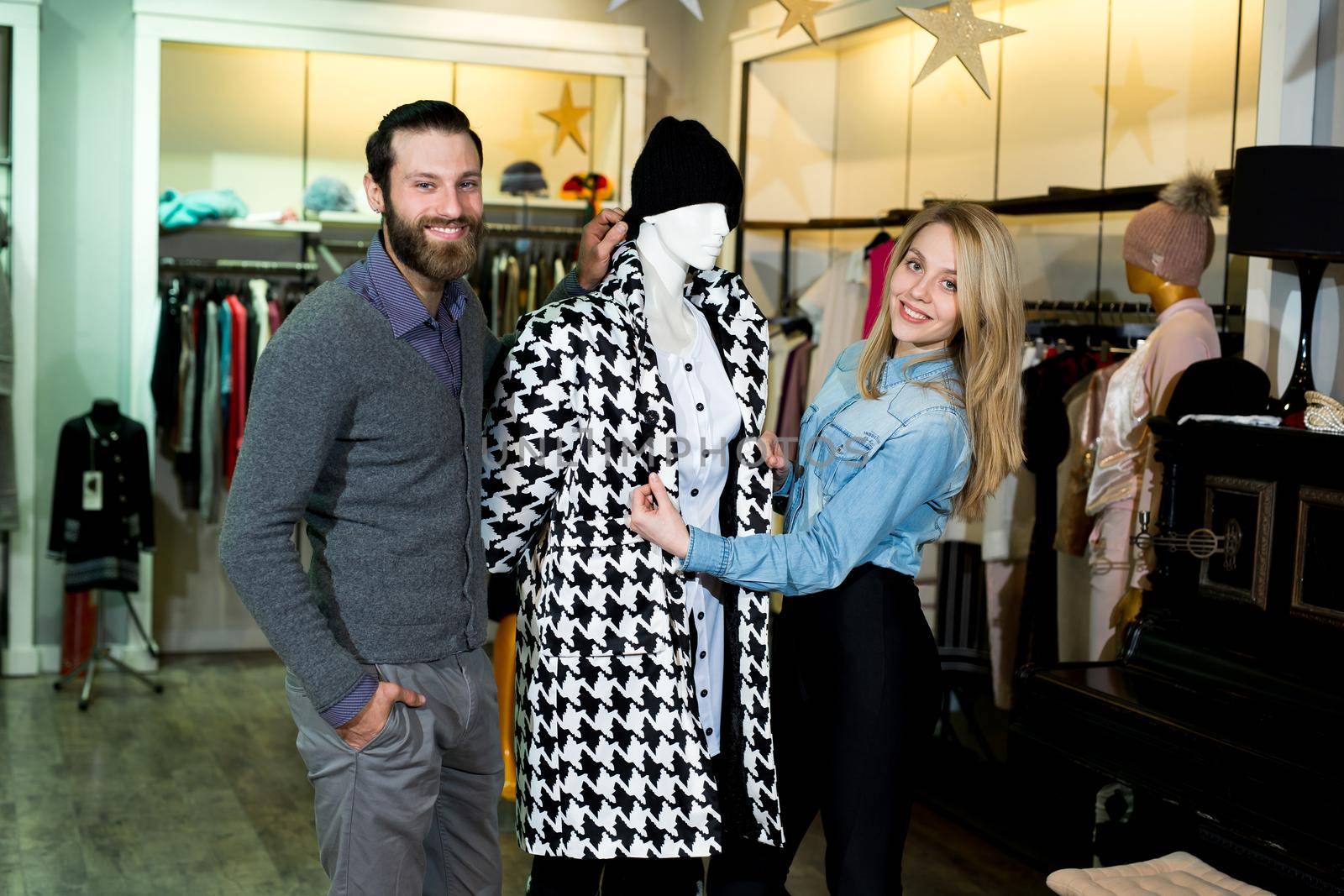 Young woman and man shopping warm jackets at the apparel store. Shopping, fashion, clothes, style and people concept - happy family trying coat on in mall or clothing store. by StudioPeace