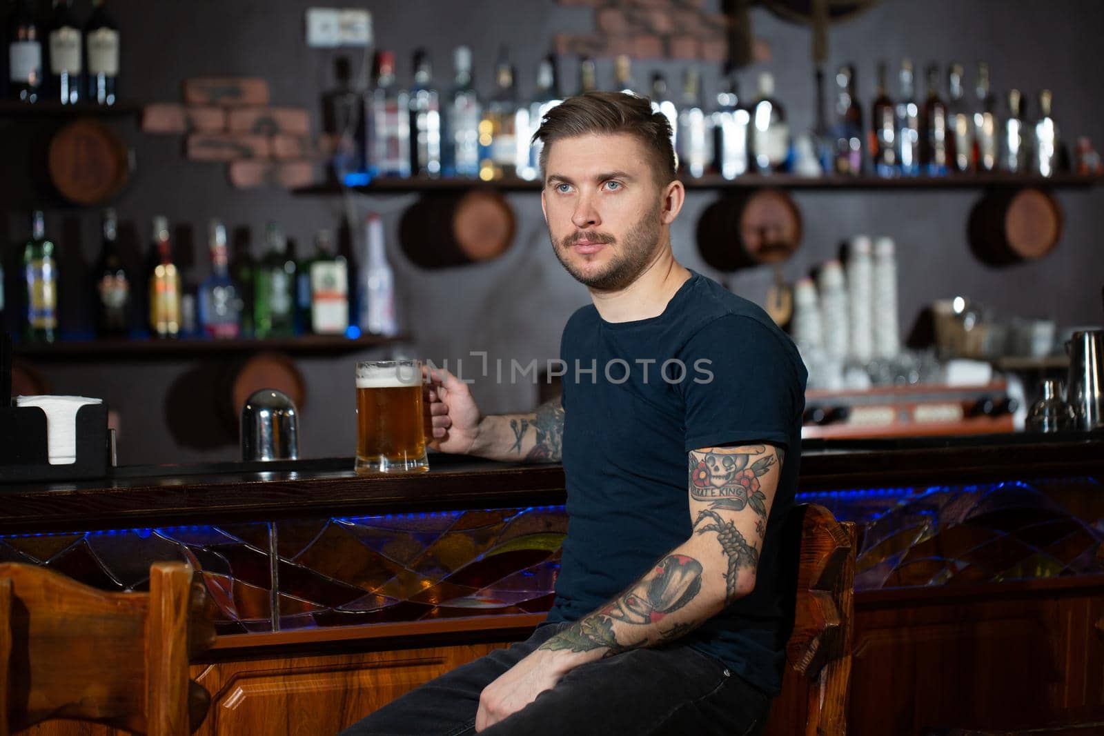 Young man sitting at bar counter with a pint of light beer. by StudioPeace