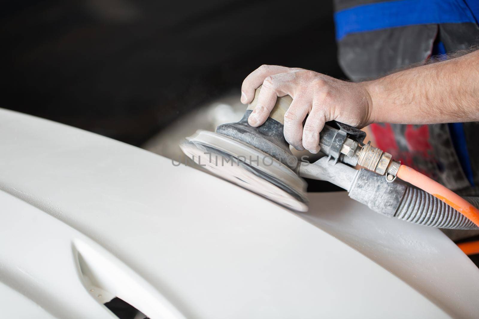 A man who sanding with a grinder and prepares the paint for the car in a car service. Repairman fix car paint by StudioPeace