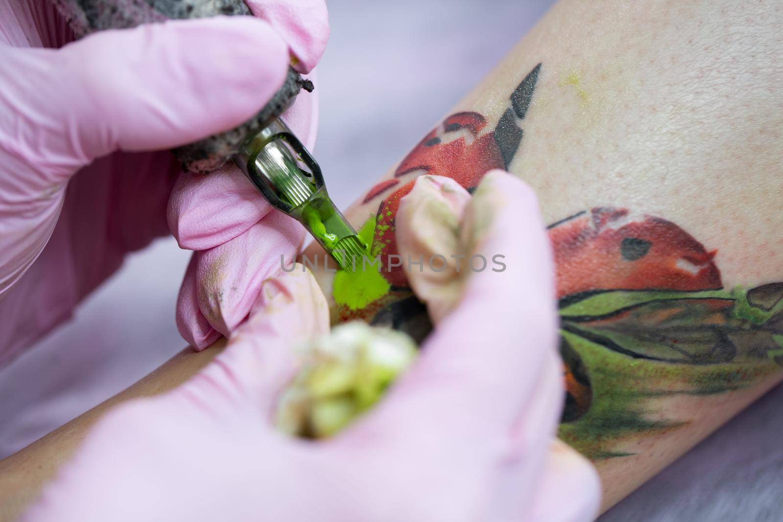 Close-up of a female artist making a color tattoo on the leg of a young girl. Tattoo artist stuffs a ladybug on a girl's leg, tattoo for a girl