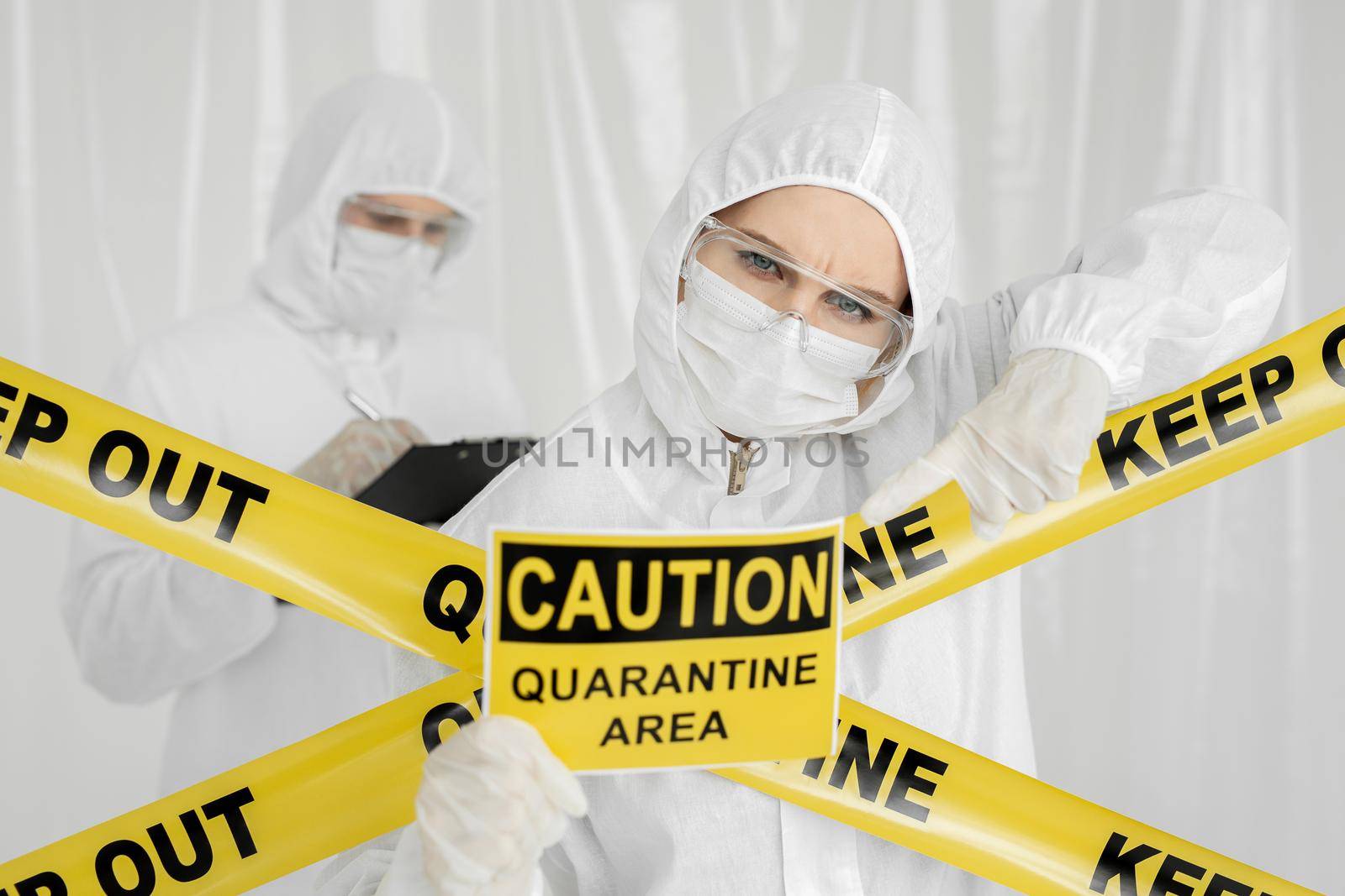 Epidemiologists a man and a woman in protective clothing are in a restricted area with a danger sign. Yellow line Keep Out Quarantine. Quarantine alert sign. Entrance is forbidden in quarantine zone. by StudioPeace