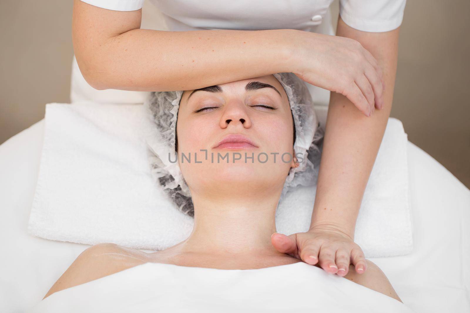 Beautician makes a professional massage of the face of the neck and shoulders for a young girl in the Spa salon. The view from the top. Facial beauty treatment. by StudioPeace