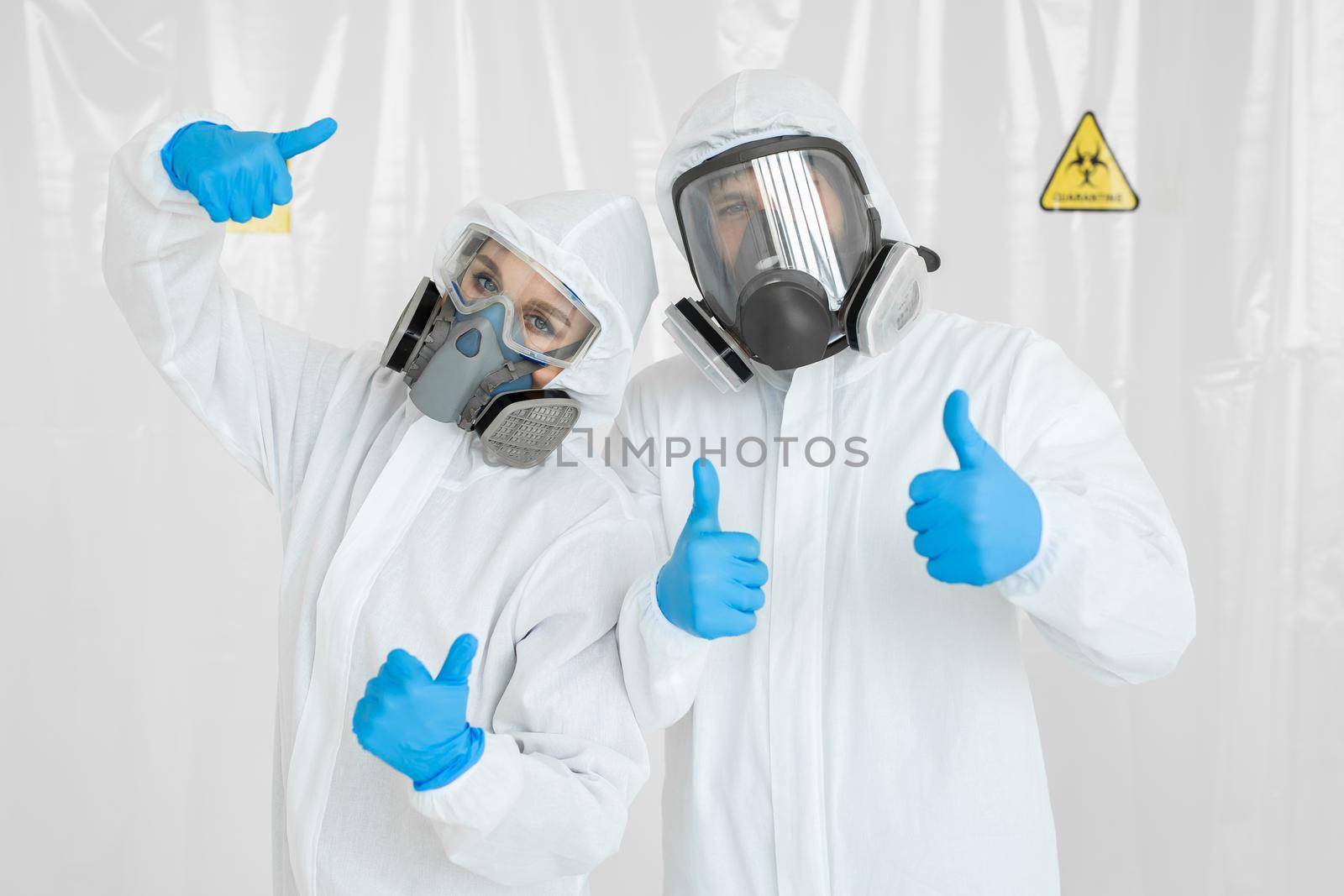 Portraits of the doctor: a man and a woman in protective suits and respirators, wearing gloves, show the thumbs up during quarantine. Covid-19 by StudioPeace