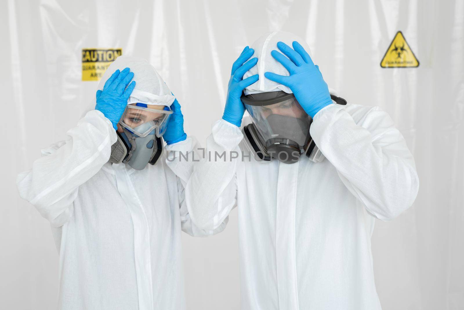 Portraits of the doctor: a man and a woman in protective suits and respirators, holding their heads during quarantine. Covid-19.