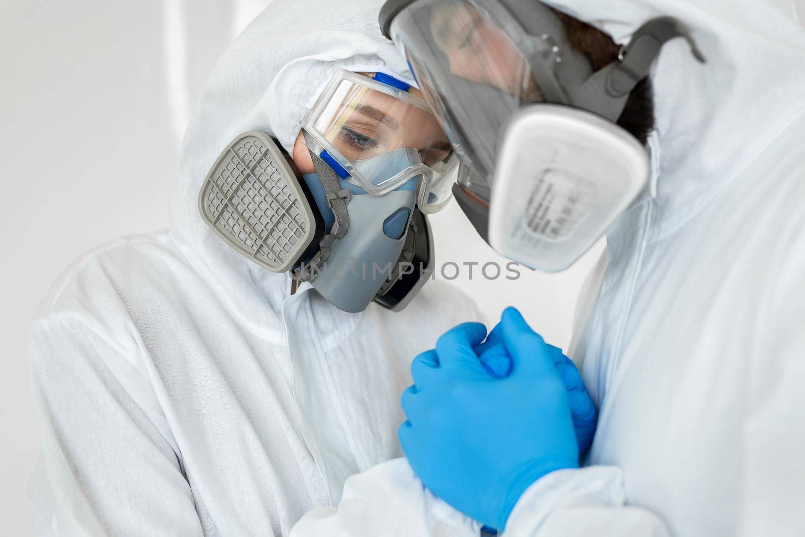 Portraits of the doctor: a man and a woman in protective suits and respirators holding hands during quarantine. Covid-19 by StudioPeace