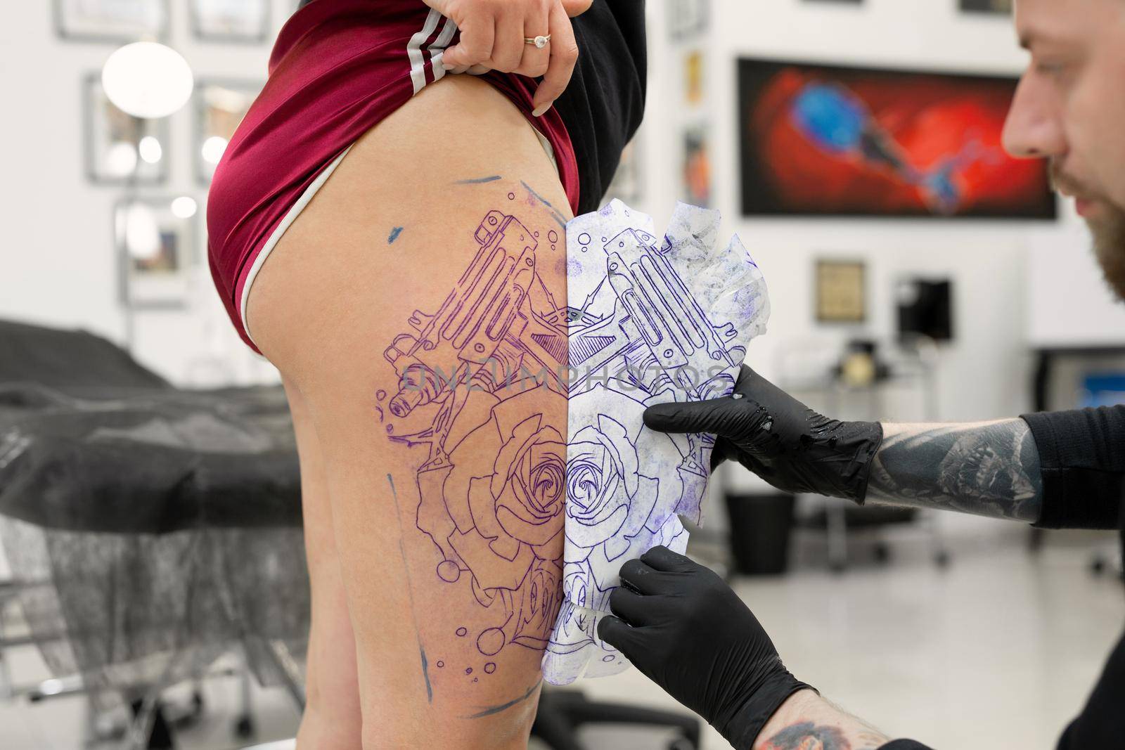 Tattoo artist transferring a tattoo sketch to a woman leg in a tattoo parlor. by StudioPeace