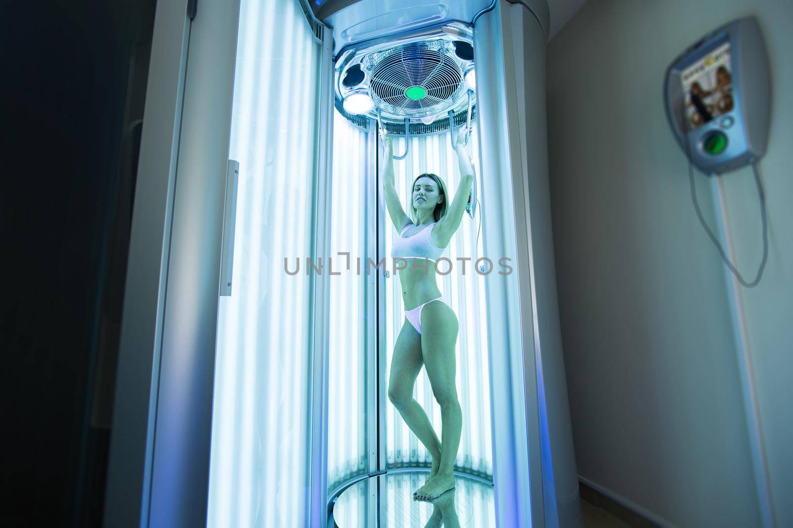 Girl with a slender body sunbathing in a modern vertical Solarium. Sexy blonde is sunbathing in the Solarium in the Spa salon