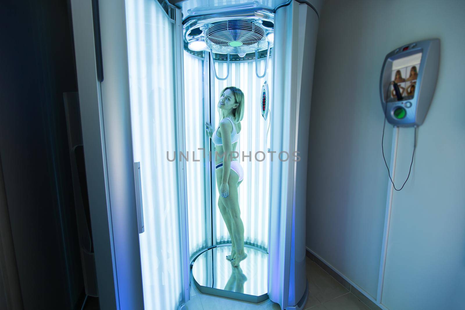 Girl with a slender body sunbathing in a modern vertical Solarium. Sexy blonde is sunbathing in the Solarium in the Spa salon