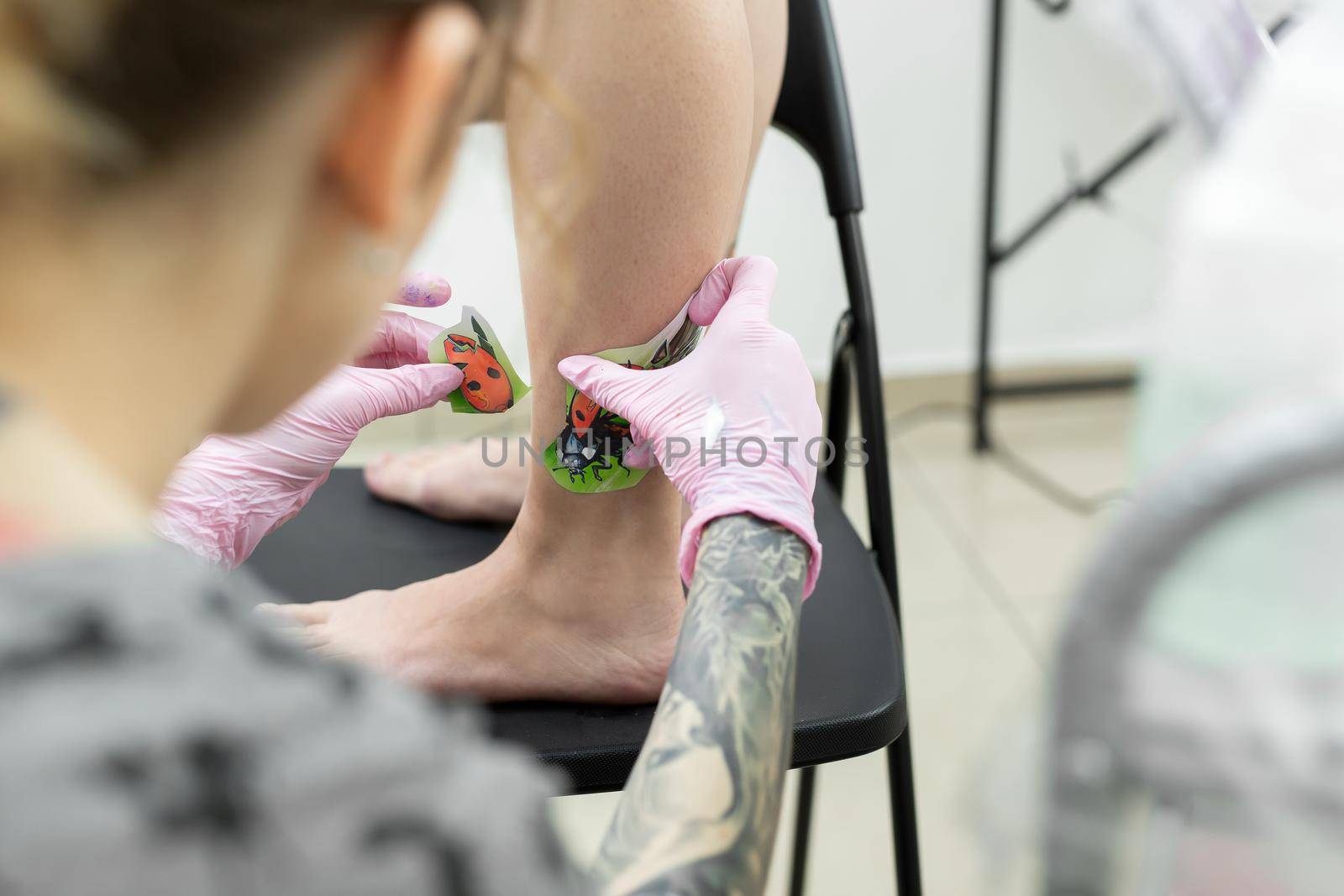 Tattoo artist puts a drawing of a ladybug on the leg of a young woman, the process of creating a tattoo. A girl takes a picture on a woman's leg. A tattoo artist makes a tattoo. Close-up.