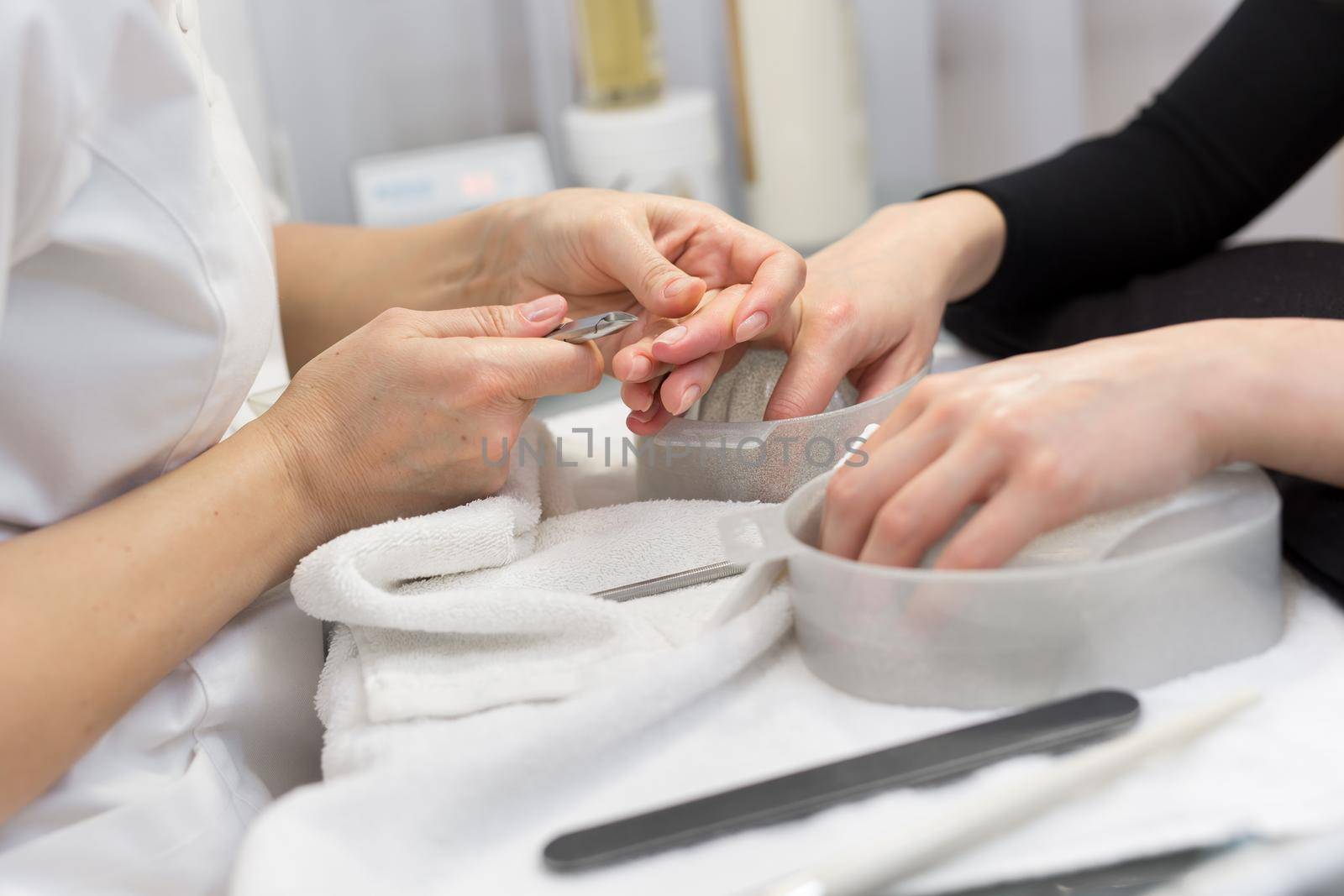 Nail Salon. Closeup Of Female Hand With Healthy Natural Nails Getting Nail Care Procedure. Hands Removing Cuticles With Professional Nail Tool, Metal Clippers. Beauty Manicure