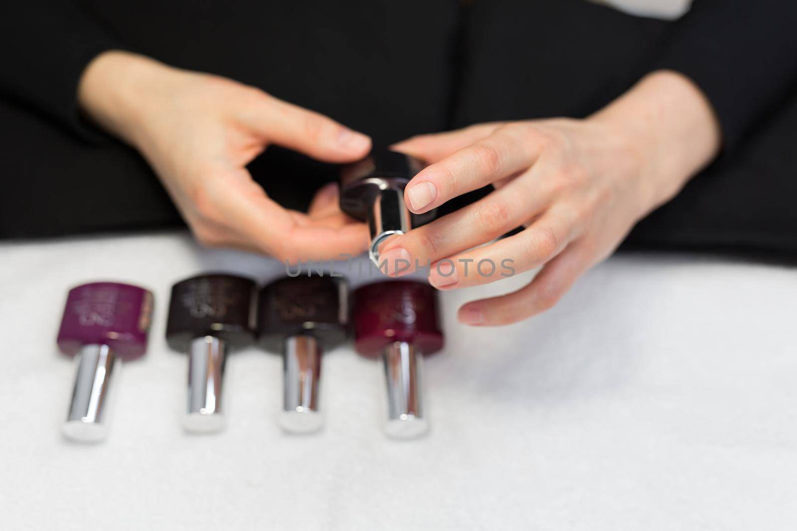 Manicure and nail care concept. A woman in a beauty salon holds colored test nail polishes with different colors and chooses the color for painting by StudioPeace