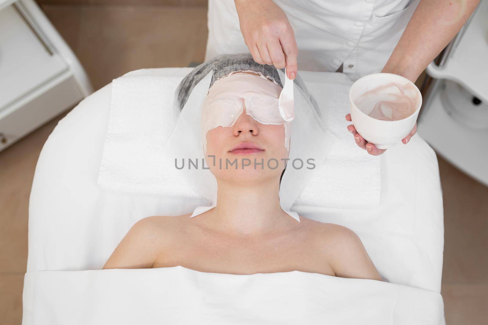 Face peeling mask, spa beauty treatment, skincare. Woman getting facial care by beautician at spa salon. Woman makes an alginate mask. Girl with a mask of beige clay. by StudioPeace
