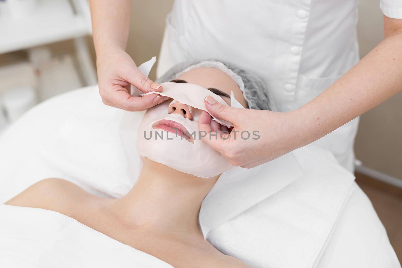 Beautician removes a clay mask from the face of a young girl in the Spa salon. Beautiful young girl at the beautician does the spa procedures. by StudioPeace