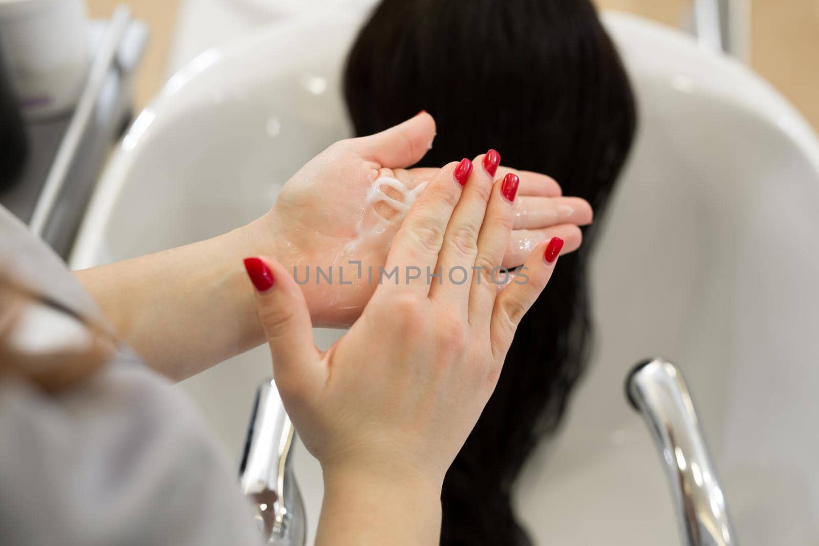 Close-up of the hand of a hairdresser who rubs moisturizing oil into the client's hair. Hairdresser applies a therapeutic mask on the girl's hair.