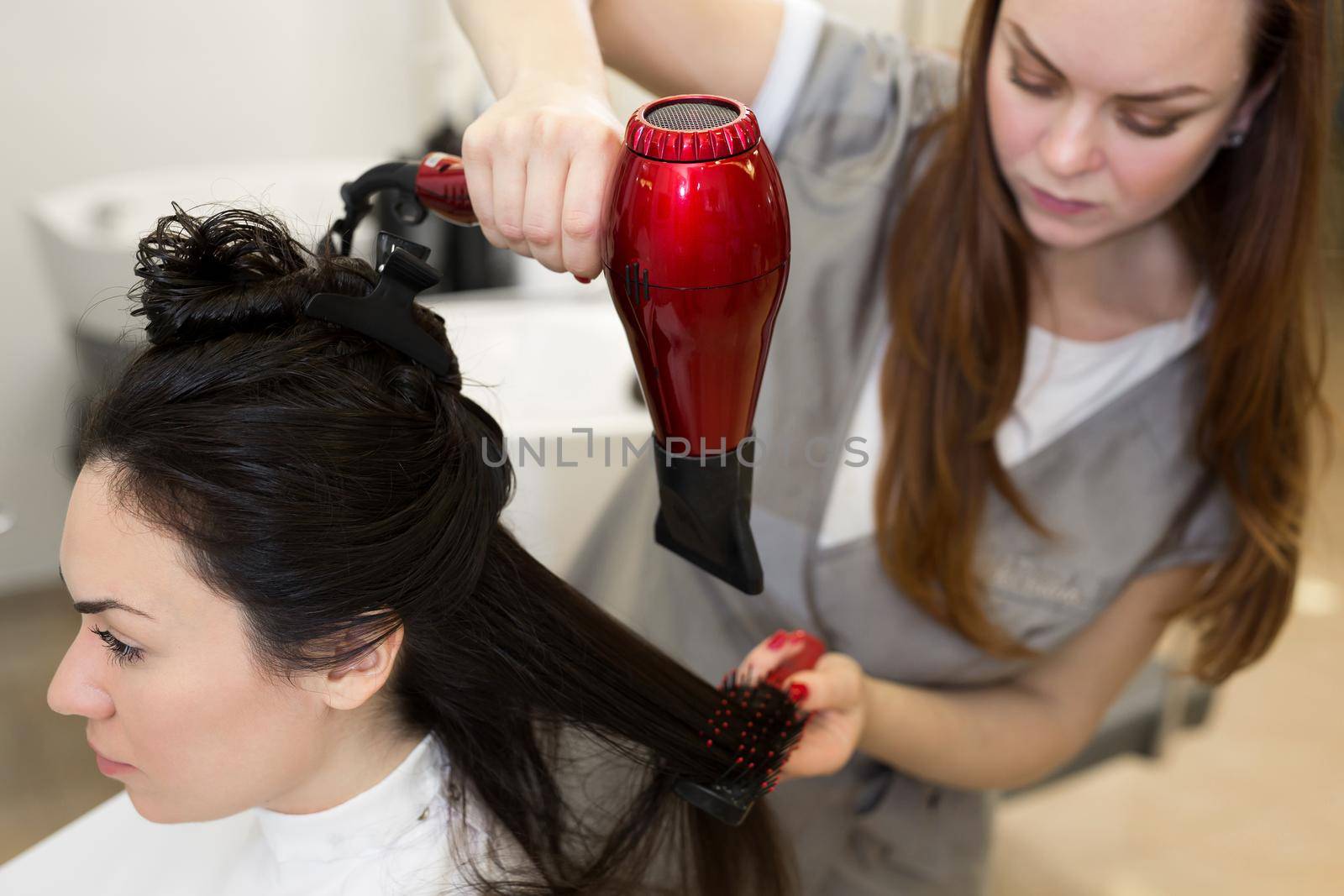 Portrait of a woman hairdresser who works with a client in a beauty salon. Hairdresser dries wet hair girl with a hair dryer. by StudioPeace
