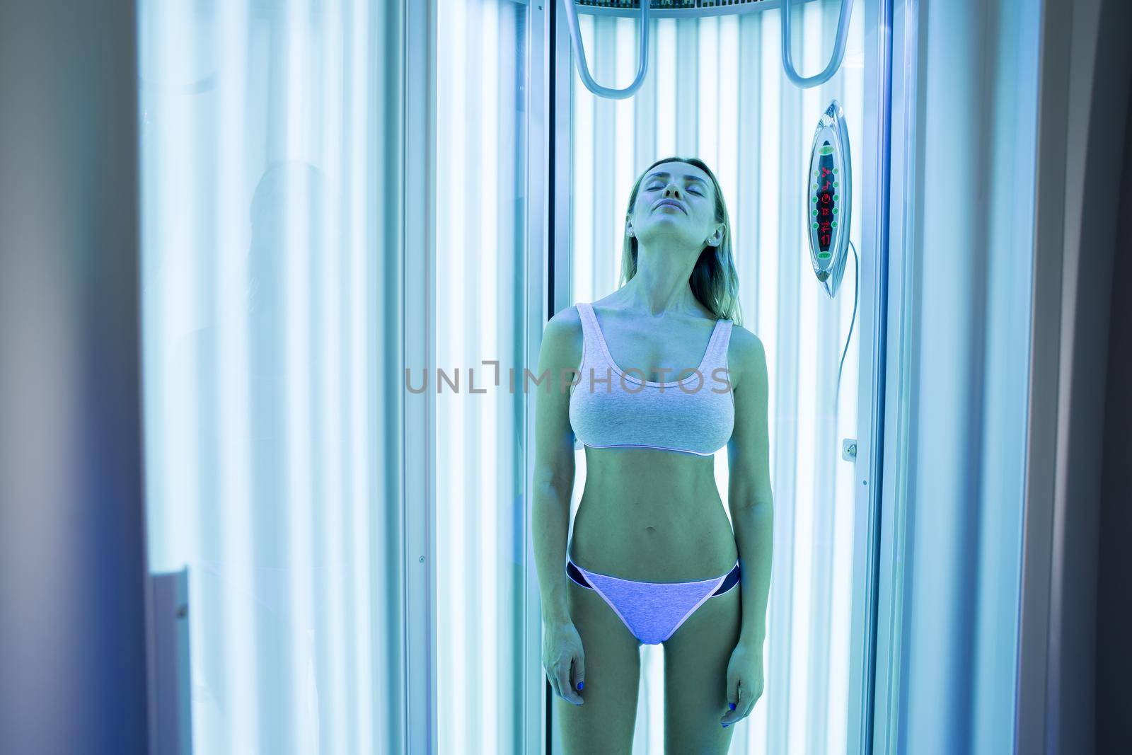Close-up of a cute elegant girl enjoying a tan in a modern solarium. Portrait of a healthy young woman in a solarium, she holds her hands up and closes her eyes with pleasure