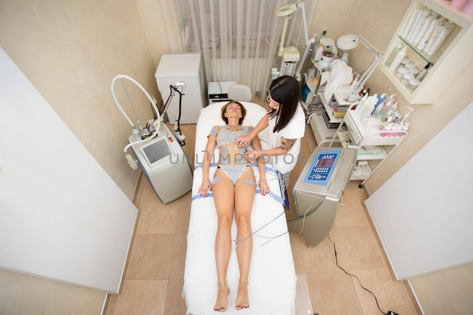 Professional beautician makes anti-cellulite massage to a young woman with the help of a biostimulating apparatus. Woman in beauty medical spa center anti-cellulite electrostimulation therapy
