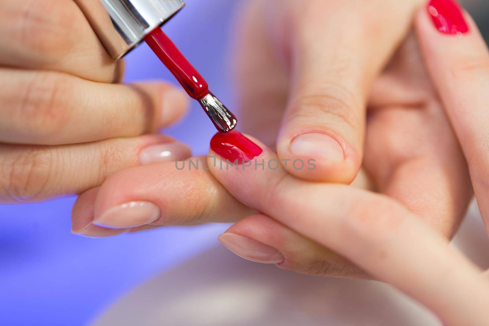 Manicurist master makes red manicure on young woman hand. Woman nail master doing nails to a girl client at a beauty salon. Care for hands