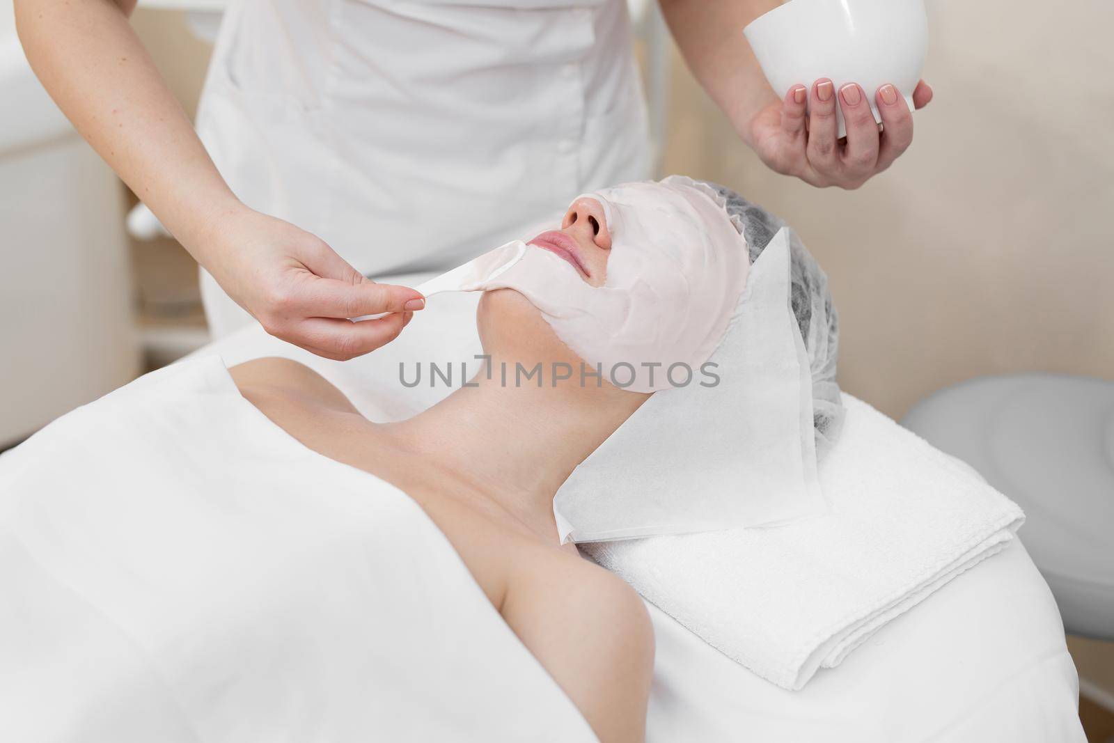 Face peeling mask, spa beauty treatment, skincare. Woman getting facial care by beautician at spa salon. Woman makes an alginate mask. Girl with a mask of beige clay. by StudioPeace