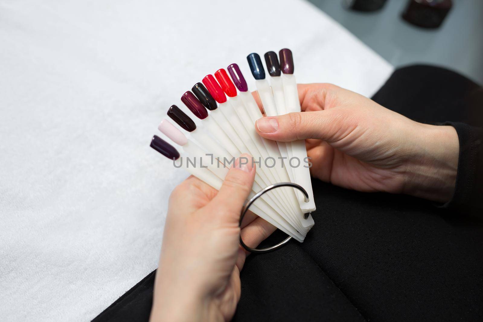Manicure and nail care concept. A woman in a beauty salon holds colored test nail polishes with different colors and chooses the color for painting by StudioPeace