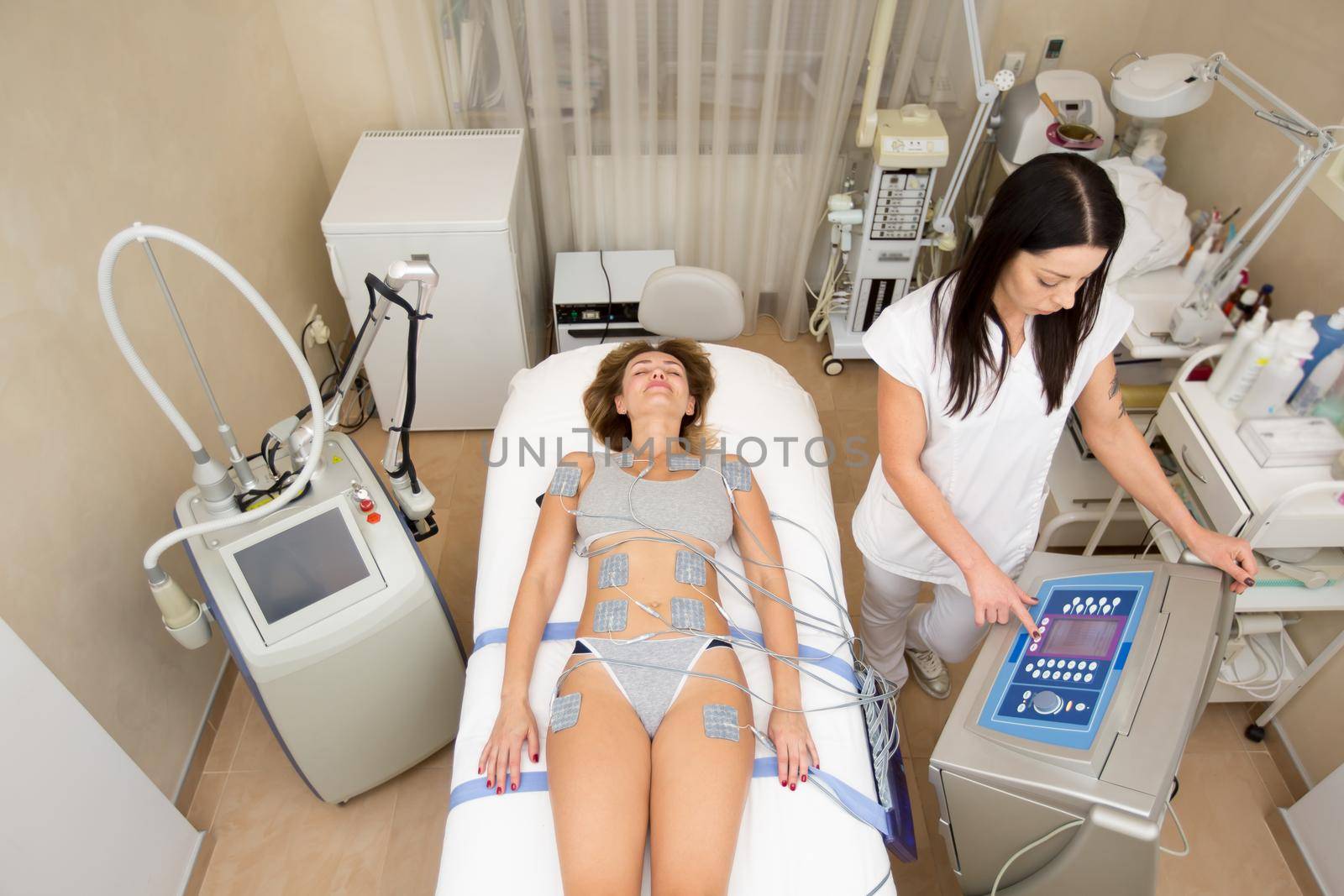 Cosmetologist works with cosmetology medical equipment, twists the lever and presses buttons on the screen. Beautician works on the biostimulation apparatus making the girl a massage. by StudioPeace