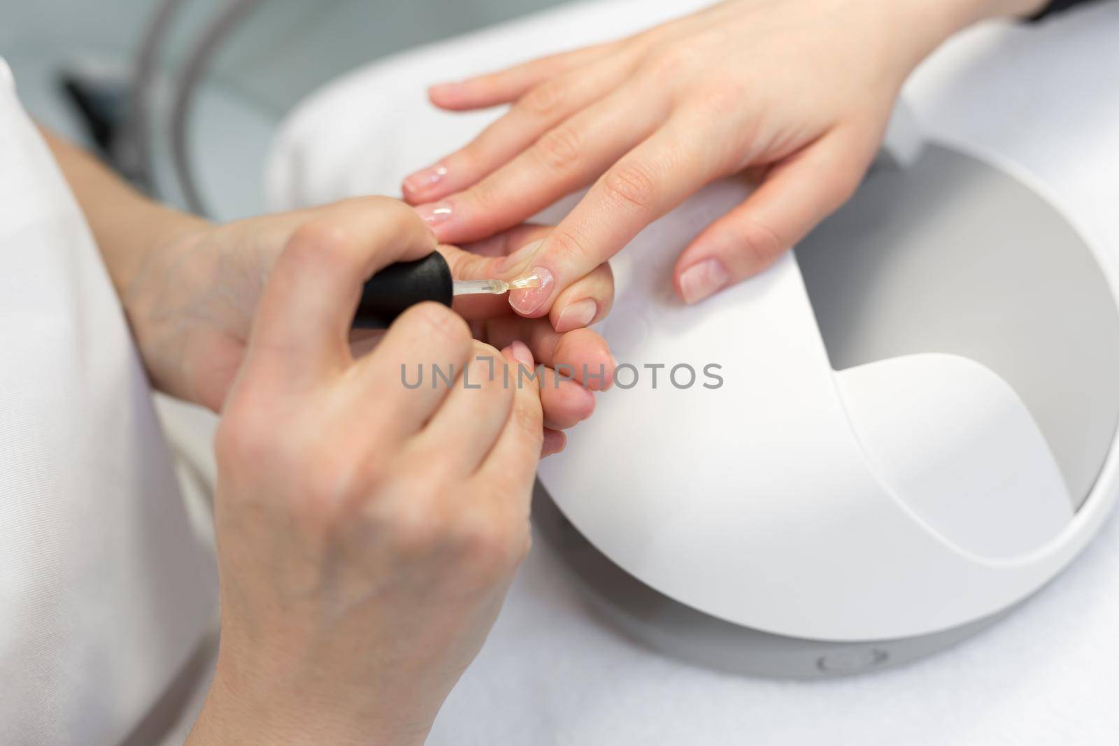 Girl paint nails in the salon of manicure, close-up. Master applies varnish on nails in manicure salon. Woman getting nail manicure in salon. Care for hands. by StudioPeace