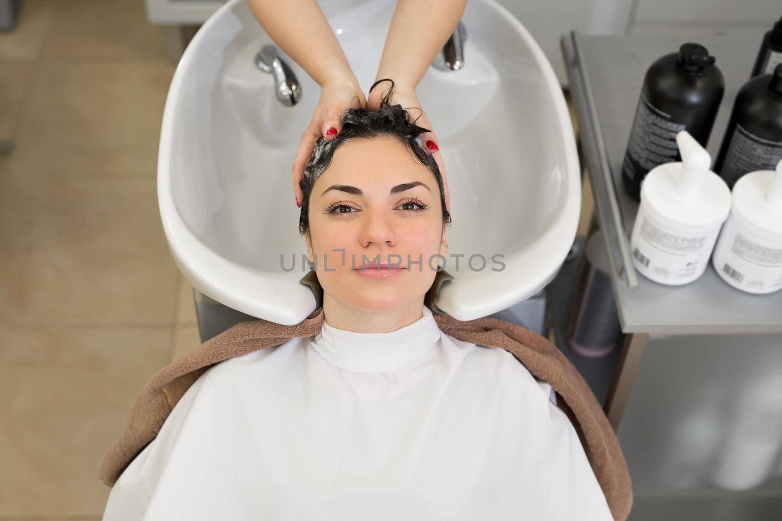 Young girl hairdresser washes her hair with shampoo and massages the head of a young woman in a modern barber salon
