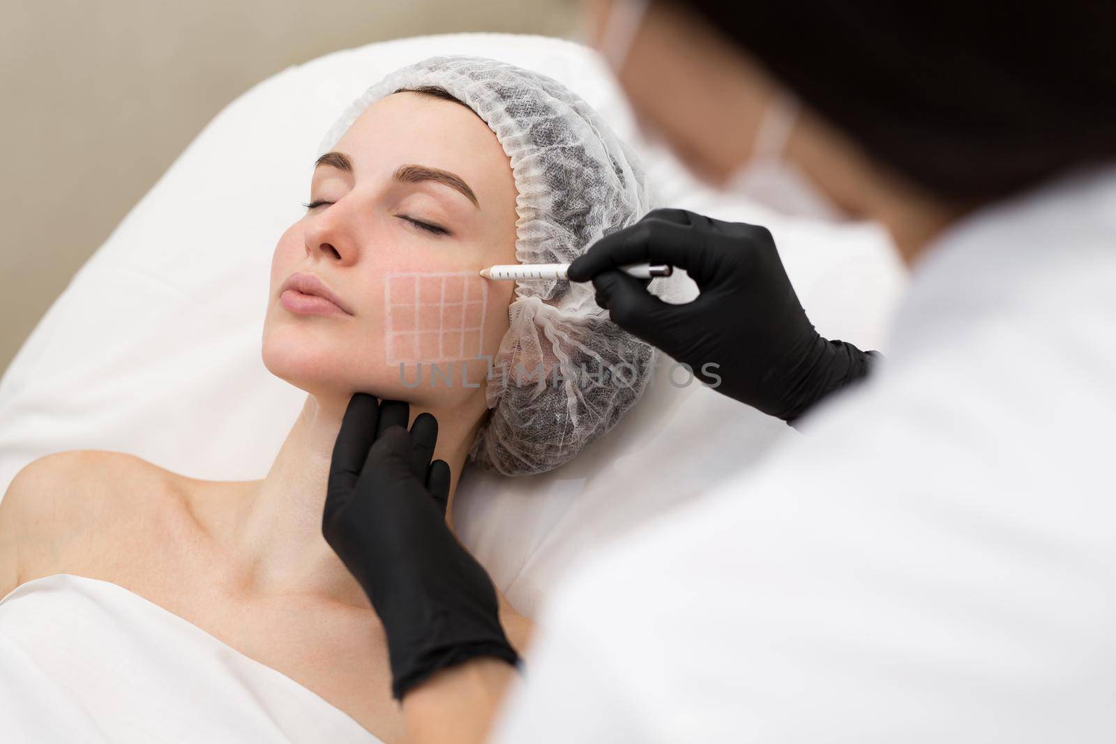 Beautician draws the contours of a white pencil on the face of the patient. Schematic marking before contouring. Close-up preparation of the face for cosmetic plastic surgery
