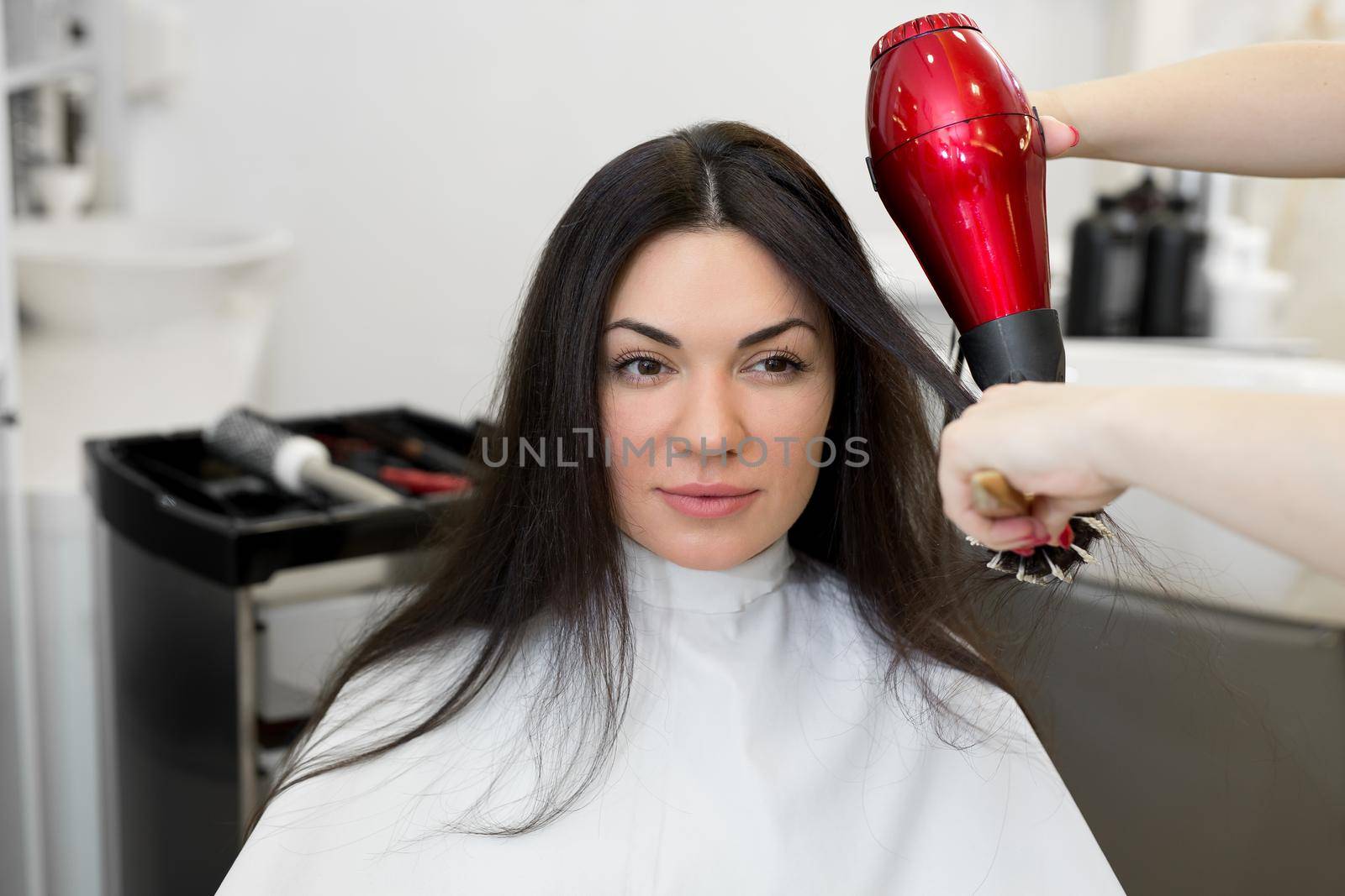Close-up of the process of hair styling in a beauty salon with a hair dryer and a comb. The hairdresser dries the girls wet hair with a hair dryer and combs the comb