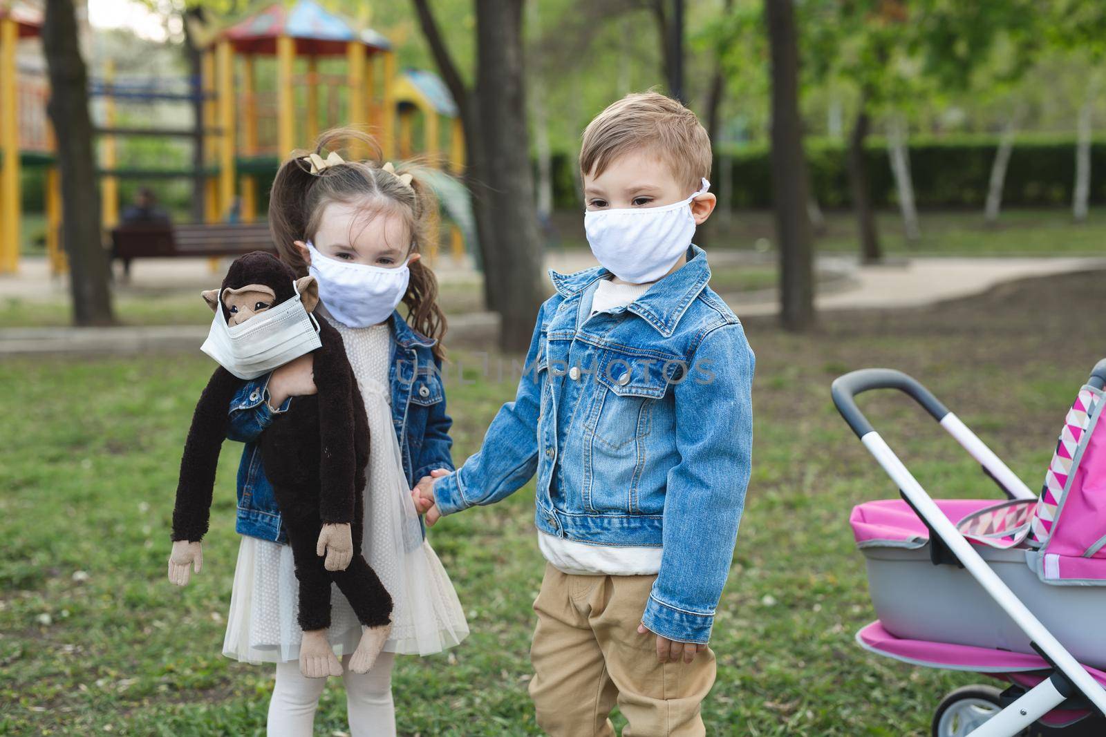 Child boy and girl walking outdoors with face mask protection. Little girl holds a stuffed monkey in her hands. Coronavirus, covid-19. by StudioPeace