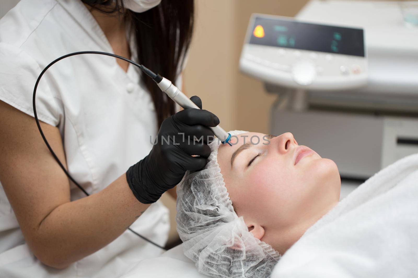 Therapist beautician makes a laser treatment to young woman's face at beauty SPA clinic. Close-up process of laser removal of blood vessels from the skin. by StudioPeace