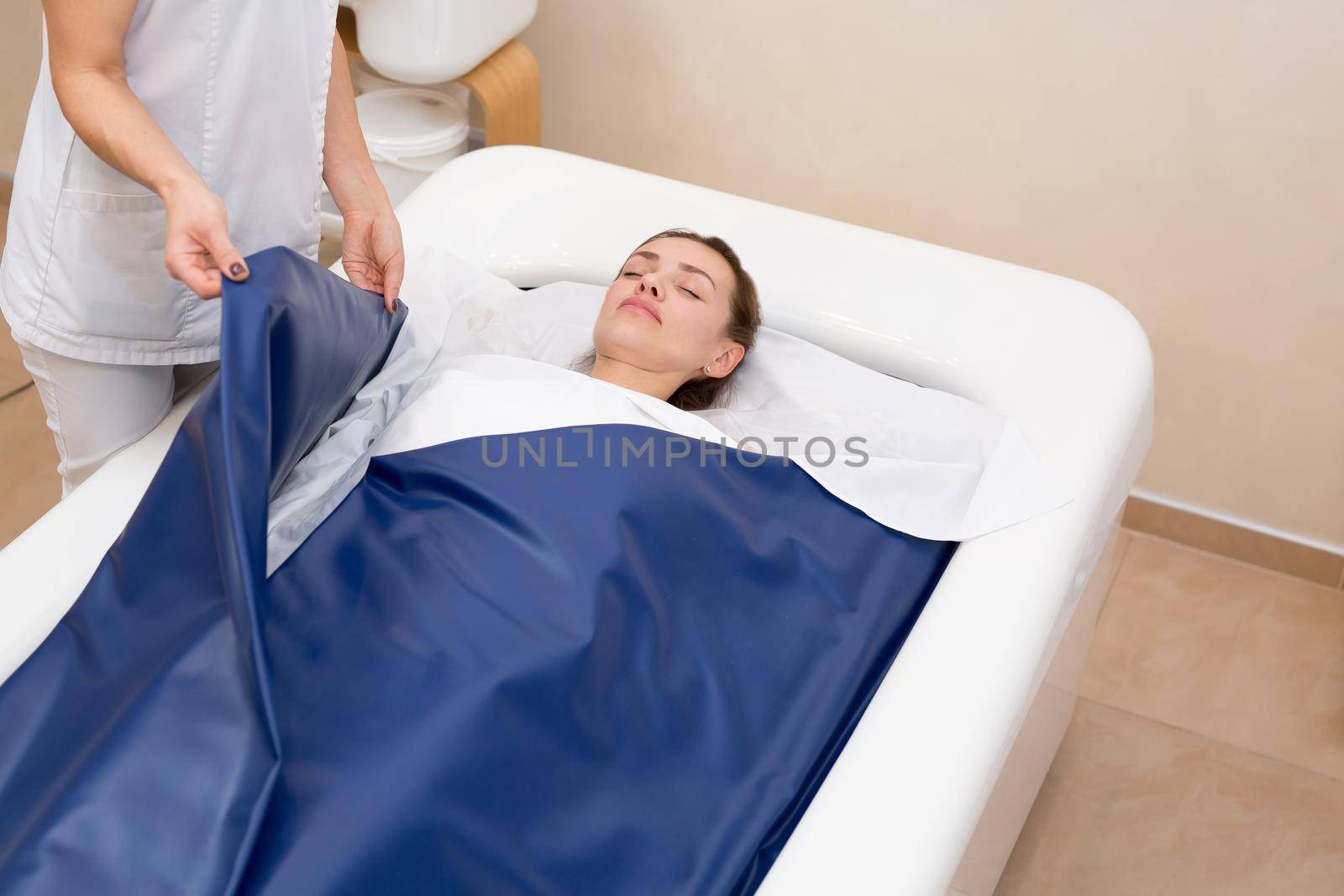 Cosmetologist covers the girl with a special blanket in the hydromassage bath. The procedure is a wrap in combination with a non-contact hot tub. Body and skin care concept. Cosmetology.