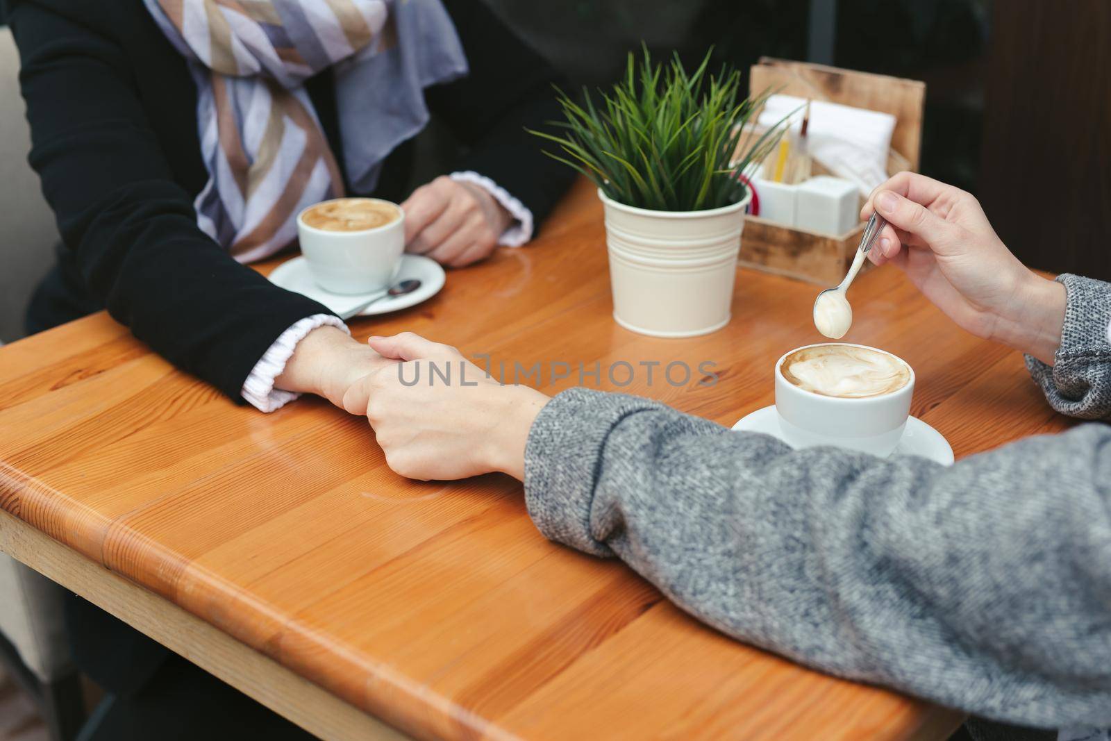 Close-up of a mother and daughter's hands on a wooden table in a cafe. Adult mother and daughter hold hands and drink coffee by StudioPeace