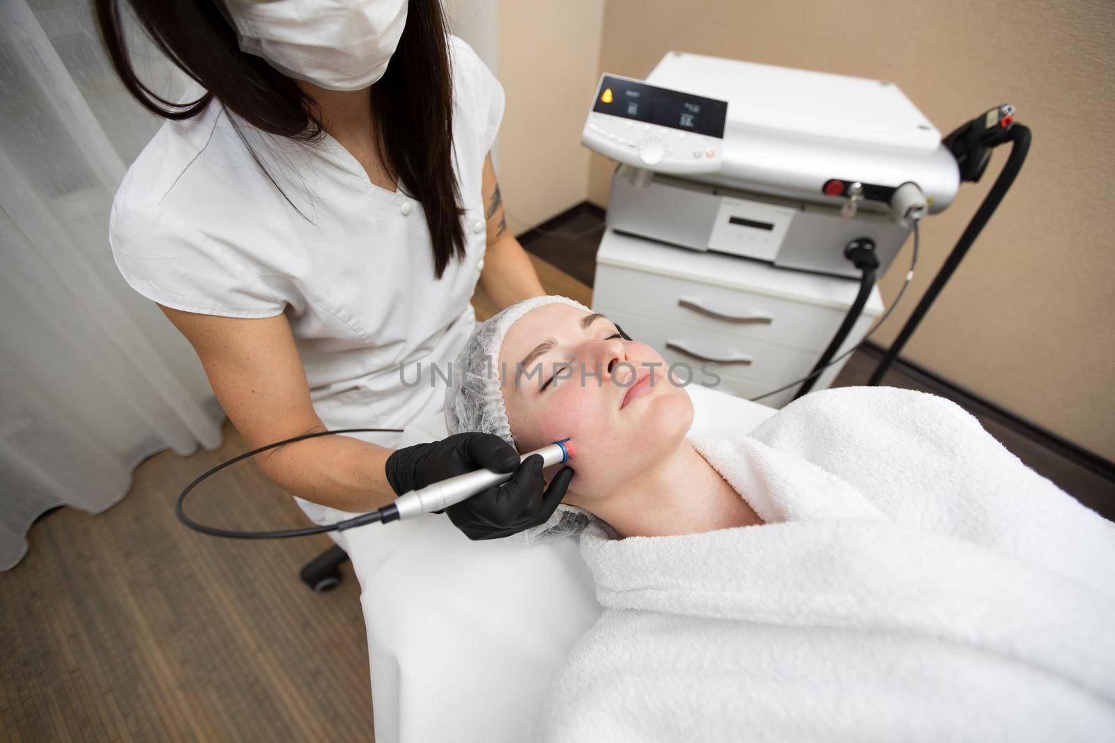 Therapist beautician makes a laser treatment to young woman's face at beauty SPA clinic. Close-up process of laser removal of blood vessels from the skin. by StudioPeace