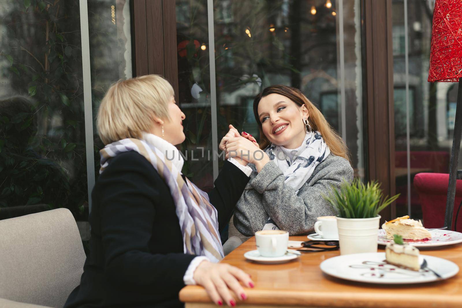 Adult daughter holds her mother's hand and smiles. Emotions of relatives in the cafe by StudioPeace