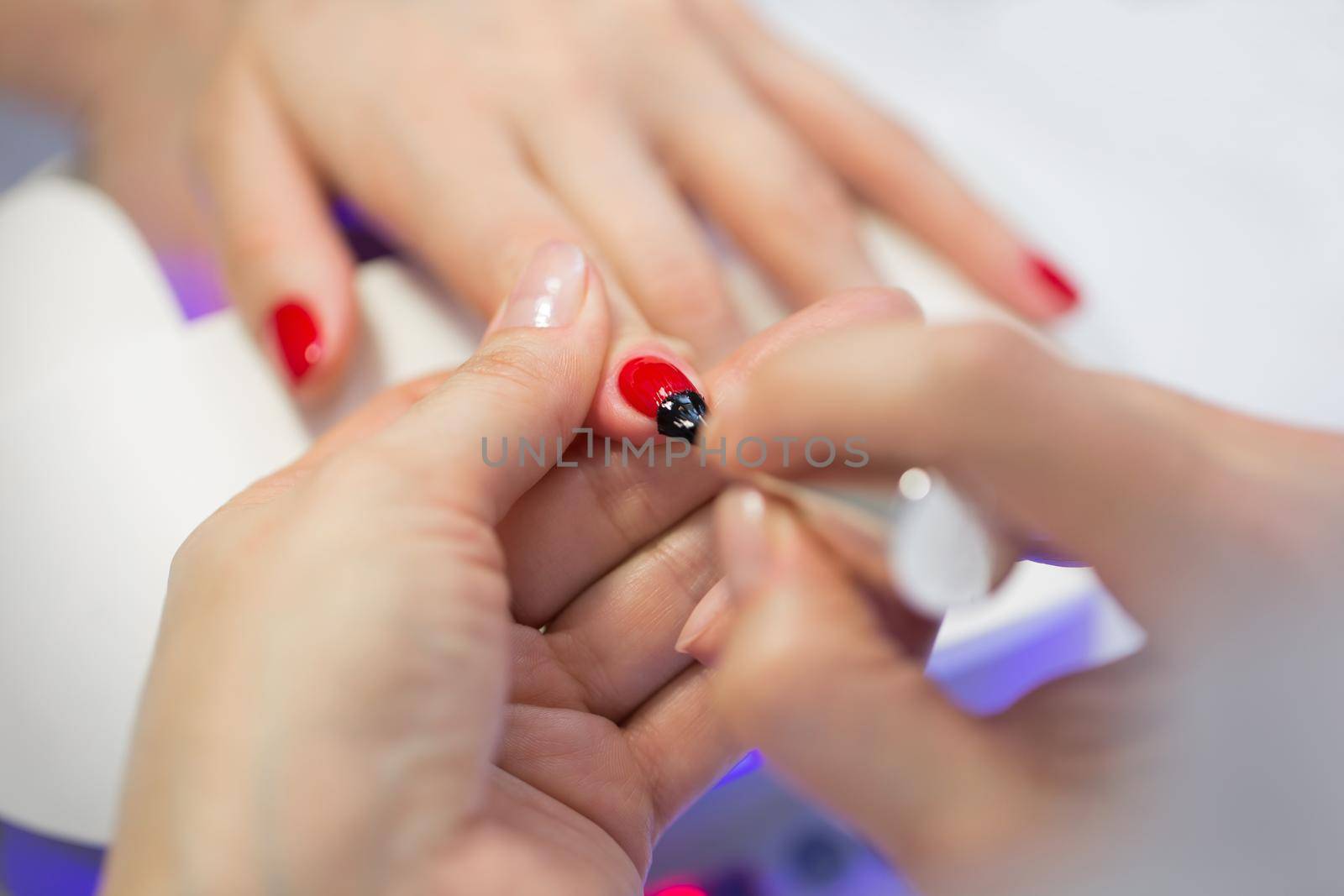 Manicurist master makes red manicure on young woman hand. Woman nail master doing nails to a girl client at a beauty salon. Care for hands