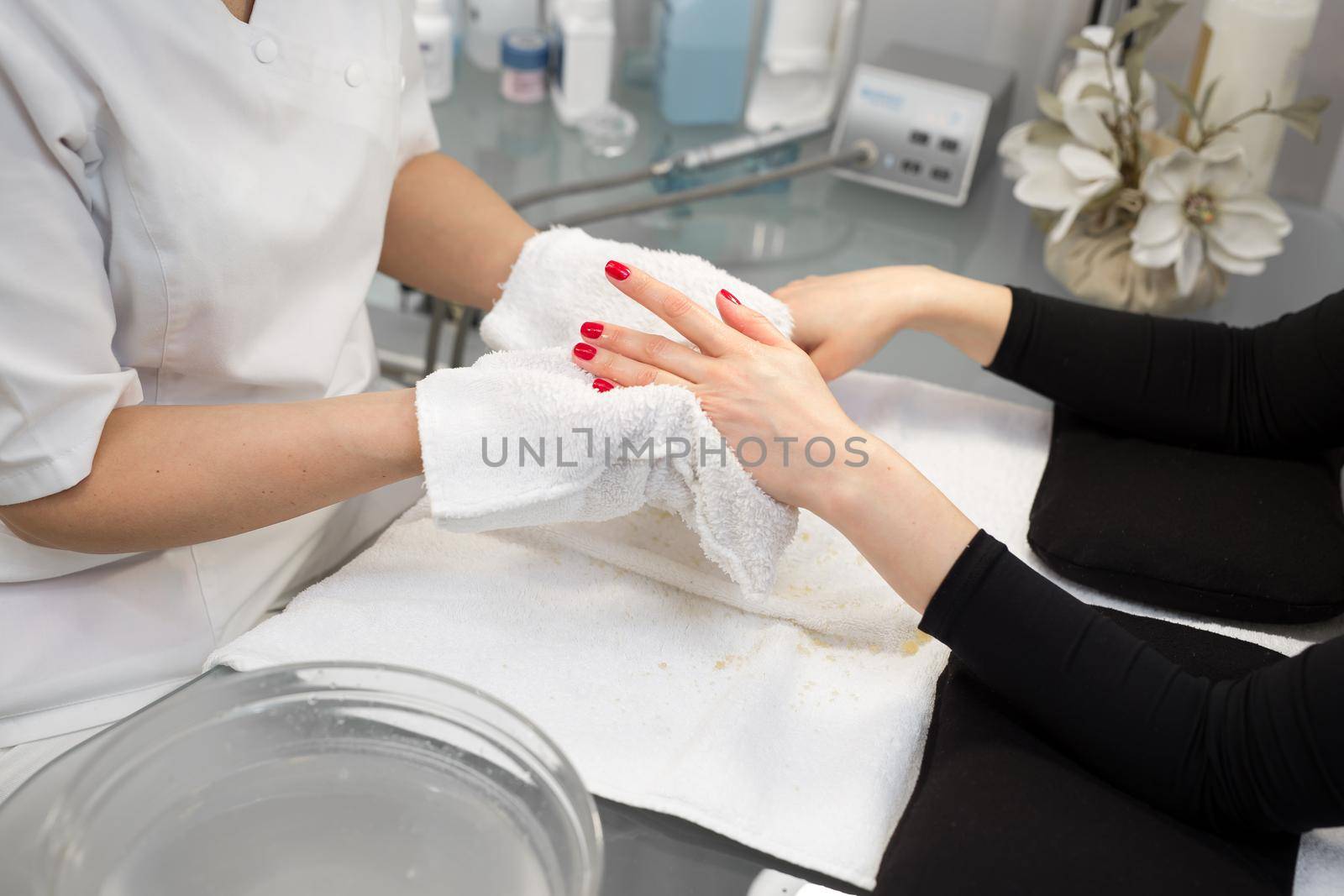 Beautician makes spa treatments for the care hands of a young girl in the beauty parlor. A manicurist wipes her hands with a wet towel to a client after scrub and massage. by StudioPeace