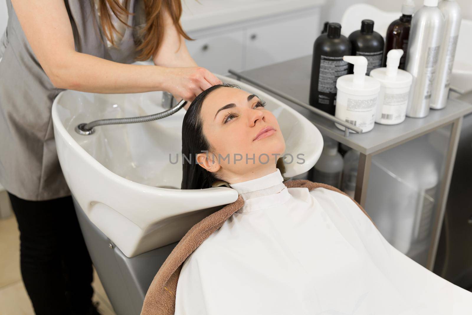 Hairdresser washes the hair of a young brunette girl before a haircut in a modern beauty salon