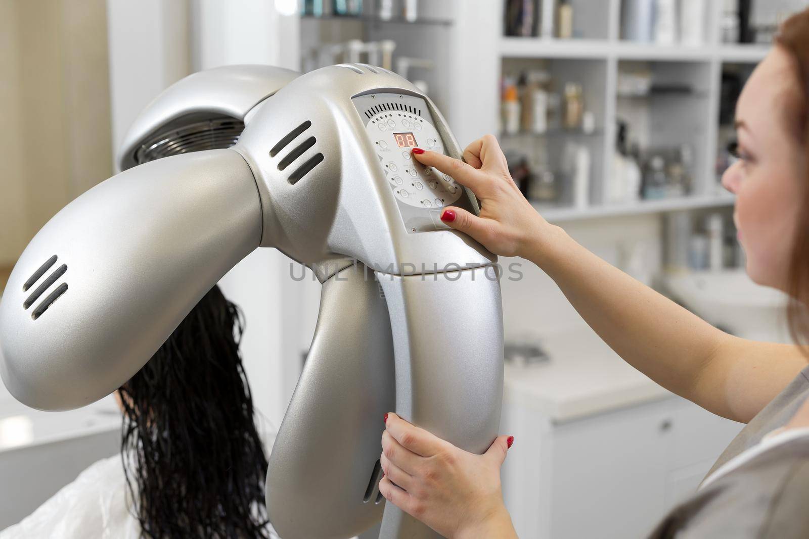 Hairdresser include hair dryer dries young girl's hair. Portrait of a girl in a beauty salon. The procedure of moisturizing hair mask in a professional hair salon