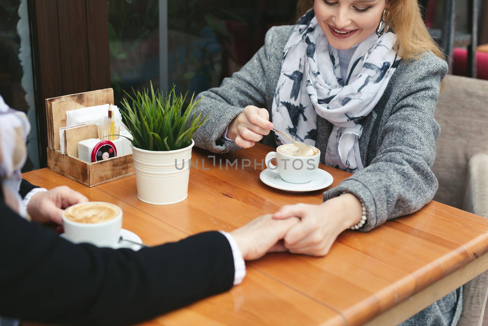 Close-up of a mother and daughter's hands on a wooden table in a cafe. Adult mother and daughter hold hands and drink coffee.