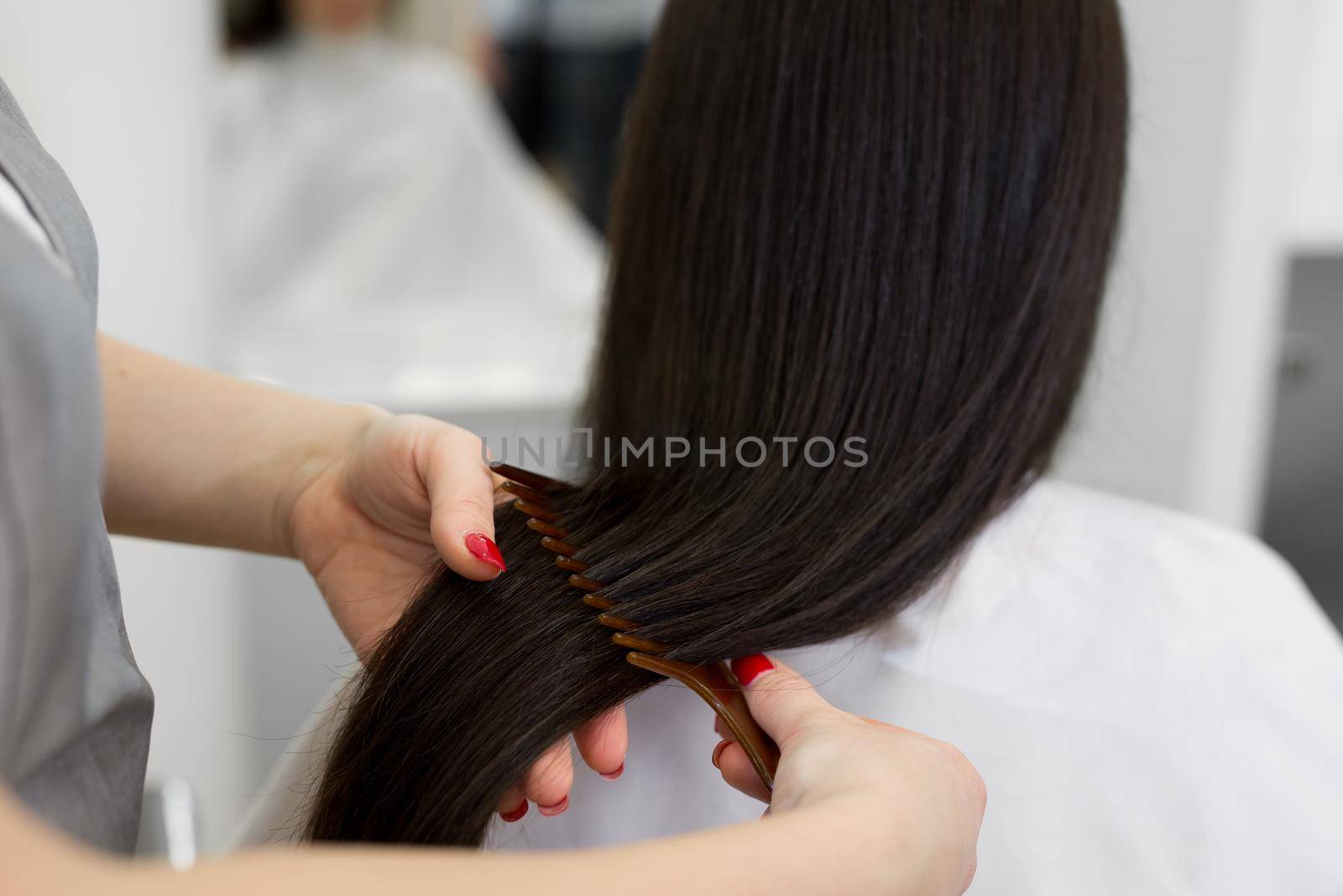 Strong, shiny and healthy long brunette hair. Hairdresser combing the hair of the client. Close-up of beautiful silky hair is in hands of stylist. by StudioPeace