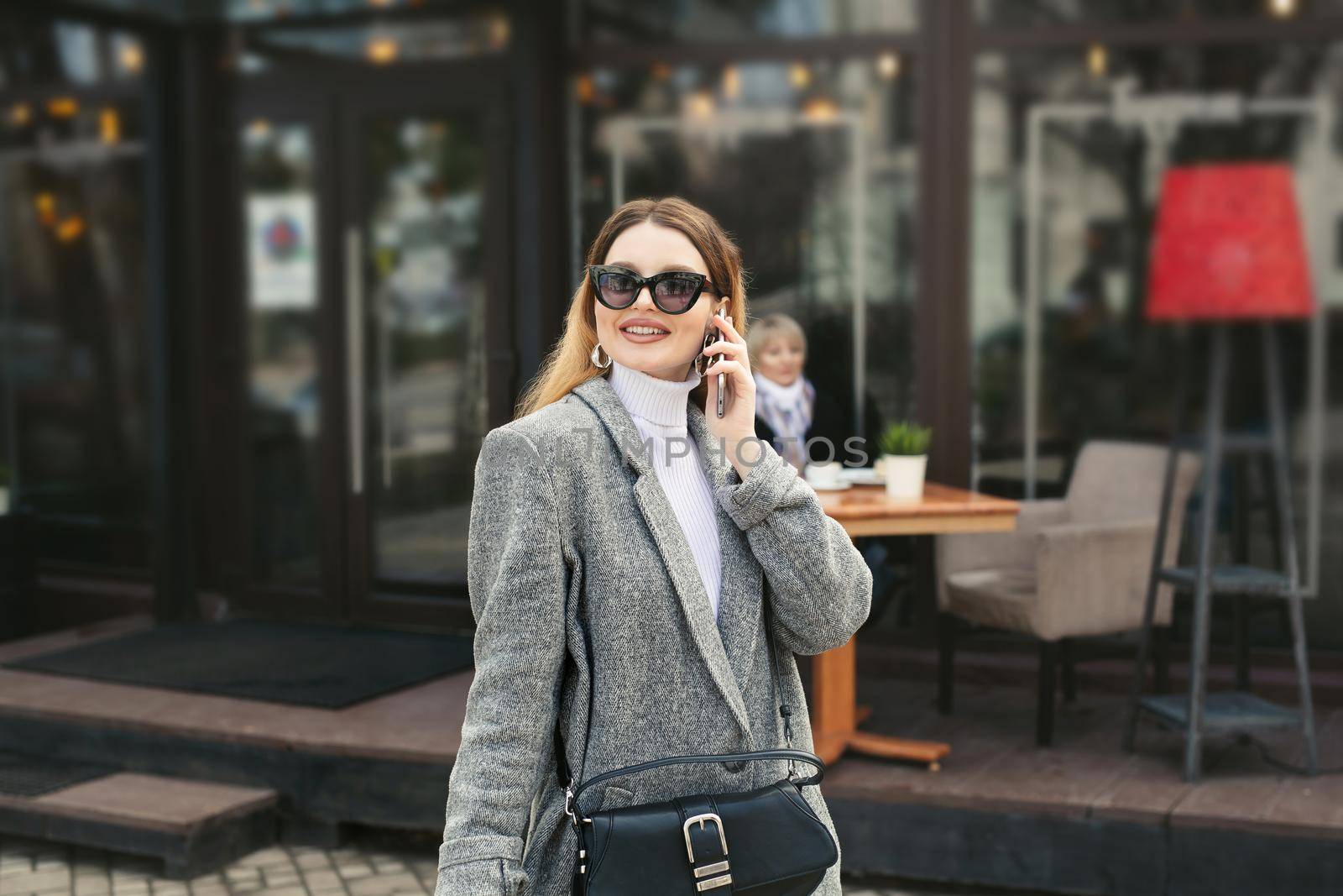 Beautiful young woman in sunglasses is talking on the phone while her elderly mother is waiting in a cafe on the street by StudioPeace