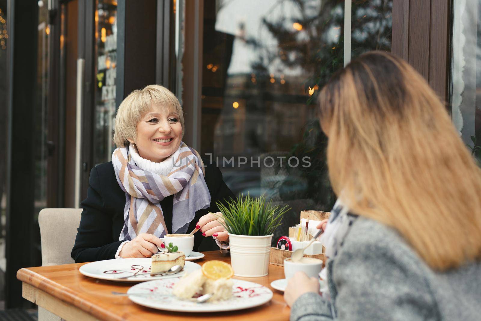 Mother and her adult daughter spending time together in cafe with coffee and desserts.
