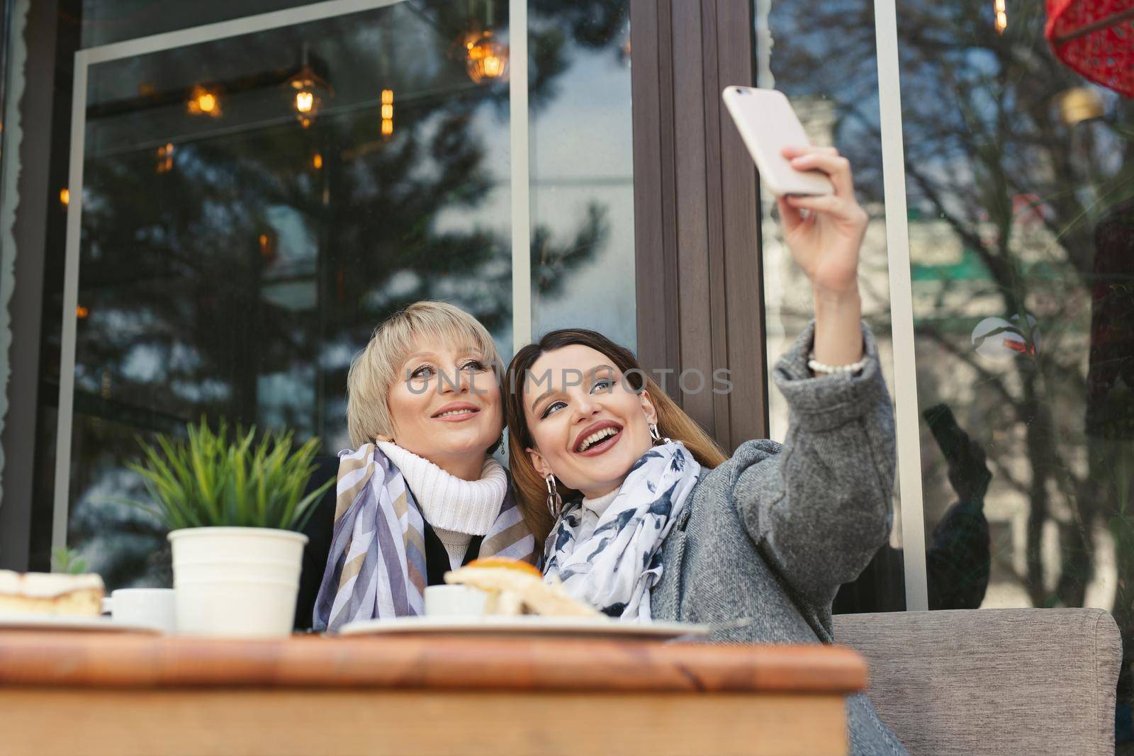 Family and technology. Aged woman and her adult daughter taking selfie on smartphone at sidewalk cafe by StudioPeace