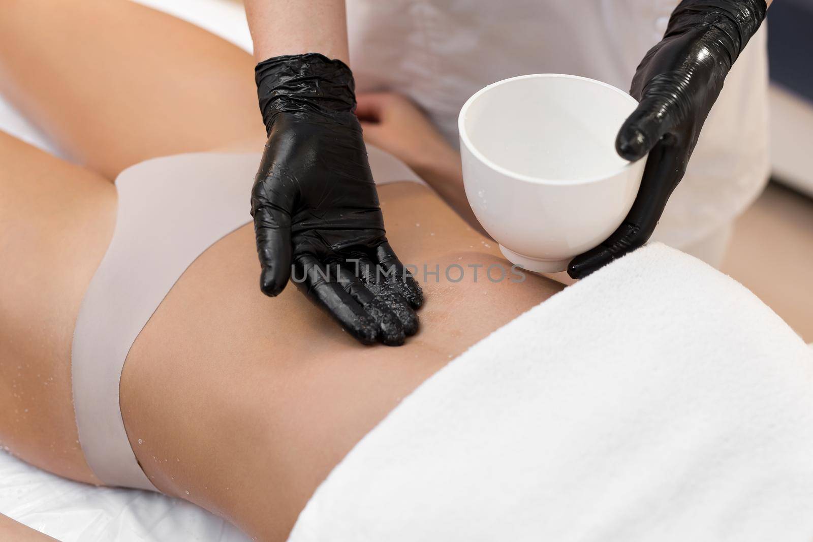 Close-up of cosmetologist doing anti-cellulite massage and peeling of the abdomen with salt to a young woman in a spa. Skin and body care concept.